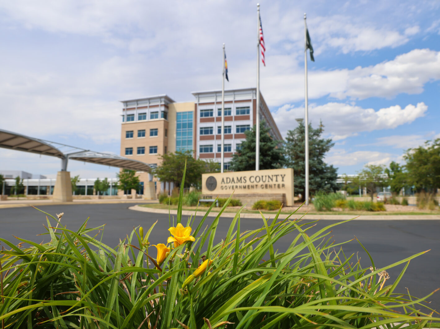 Adams County Government Center front entrance with flags and yellow flowers in foreground