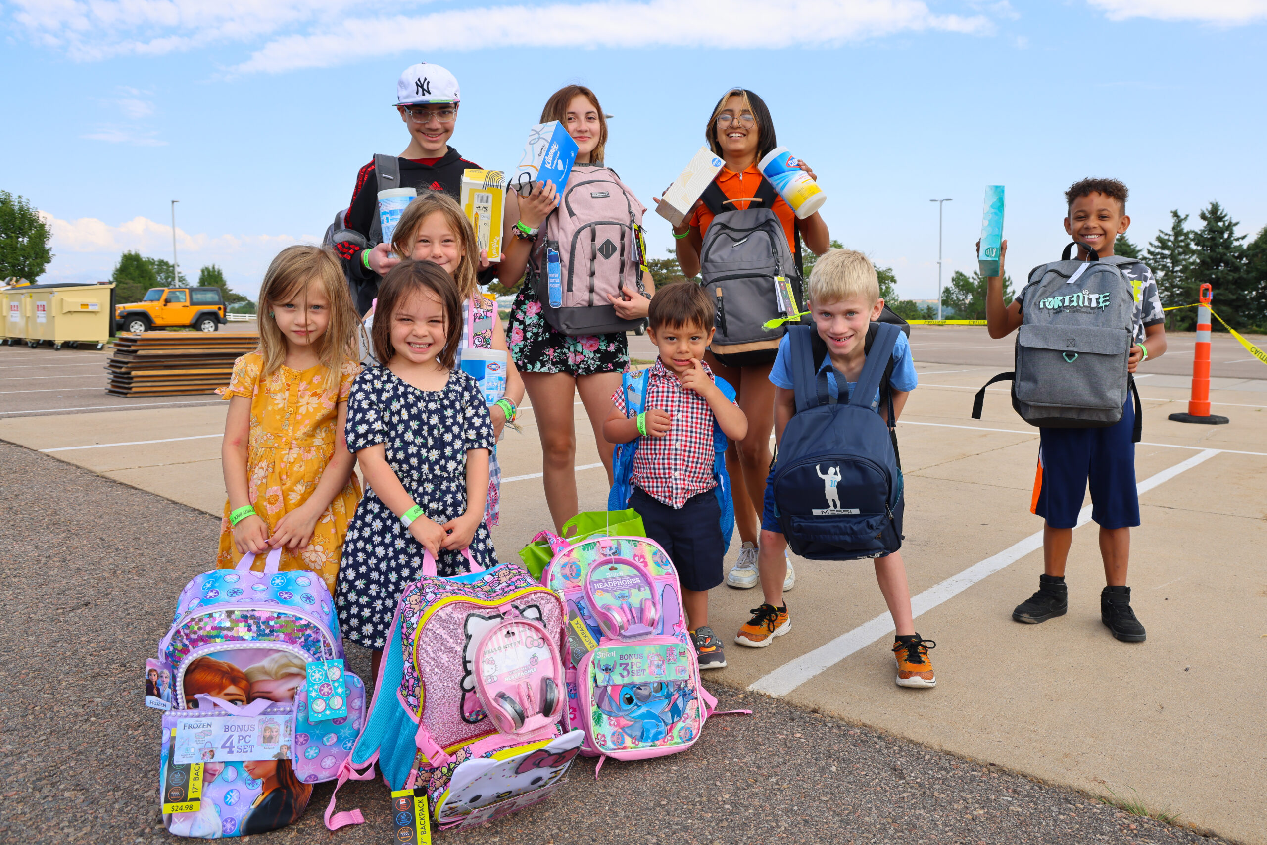 Children holding backpacks and school supplies, smiling at an outdoor event. Fortnite logos visible.