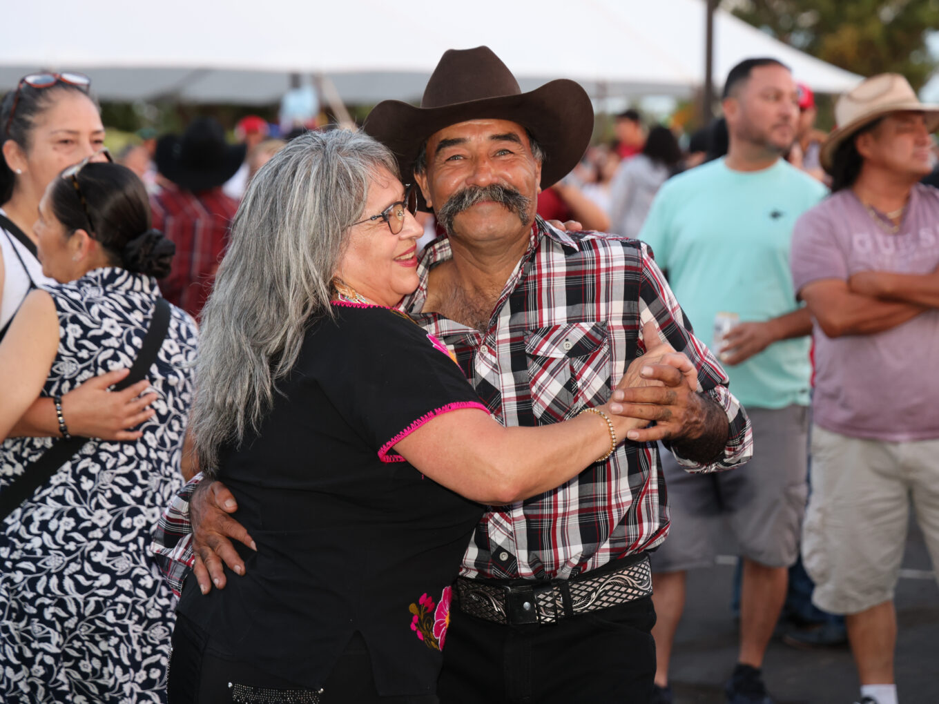 Couple dancing joyfully at a lively outdoor event, surrounded by onlookers.