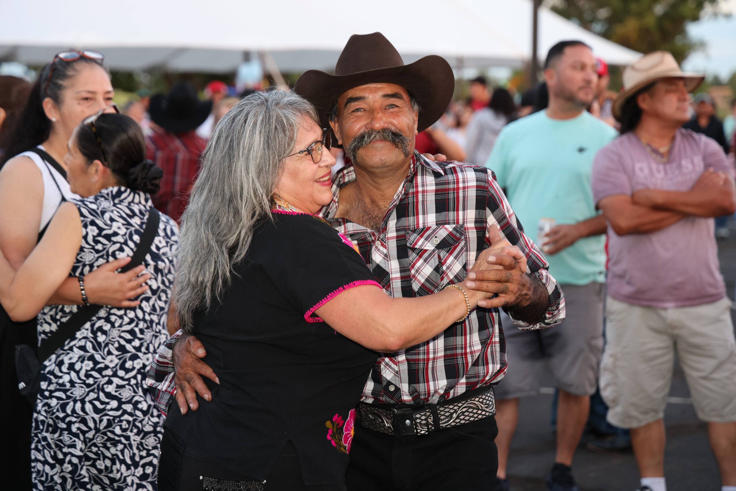 Couple dancing joyfully at a lively outdoor event, surrounded by onlookers.