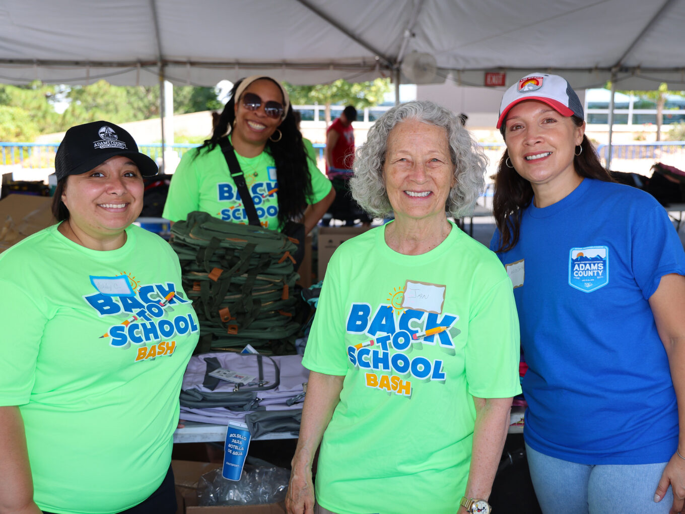 Four people smiling at Back to School Bash, wearing vibrant event T-shirts