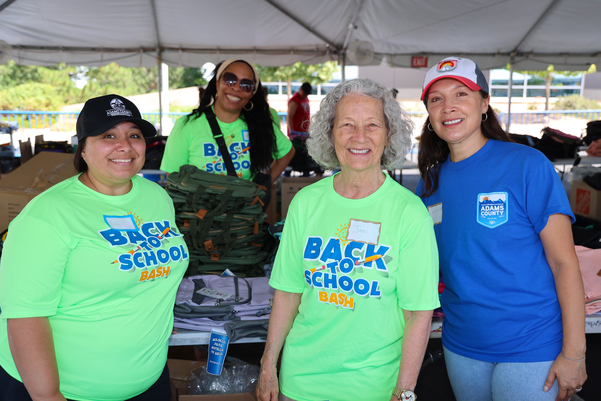 Four people smiling at Back to School Bash, wearing vibrant event T-shirts