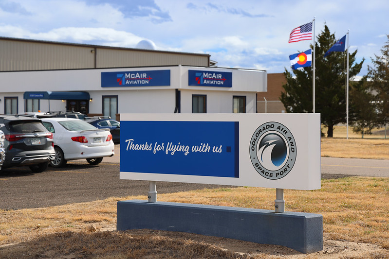 Thanks for flying with us sign at Colorado Air and Space Port with McAir Aviation building and parked cars.