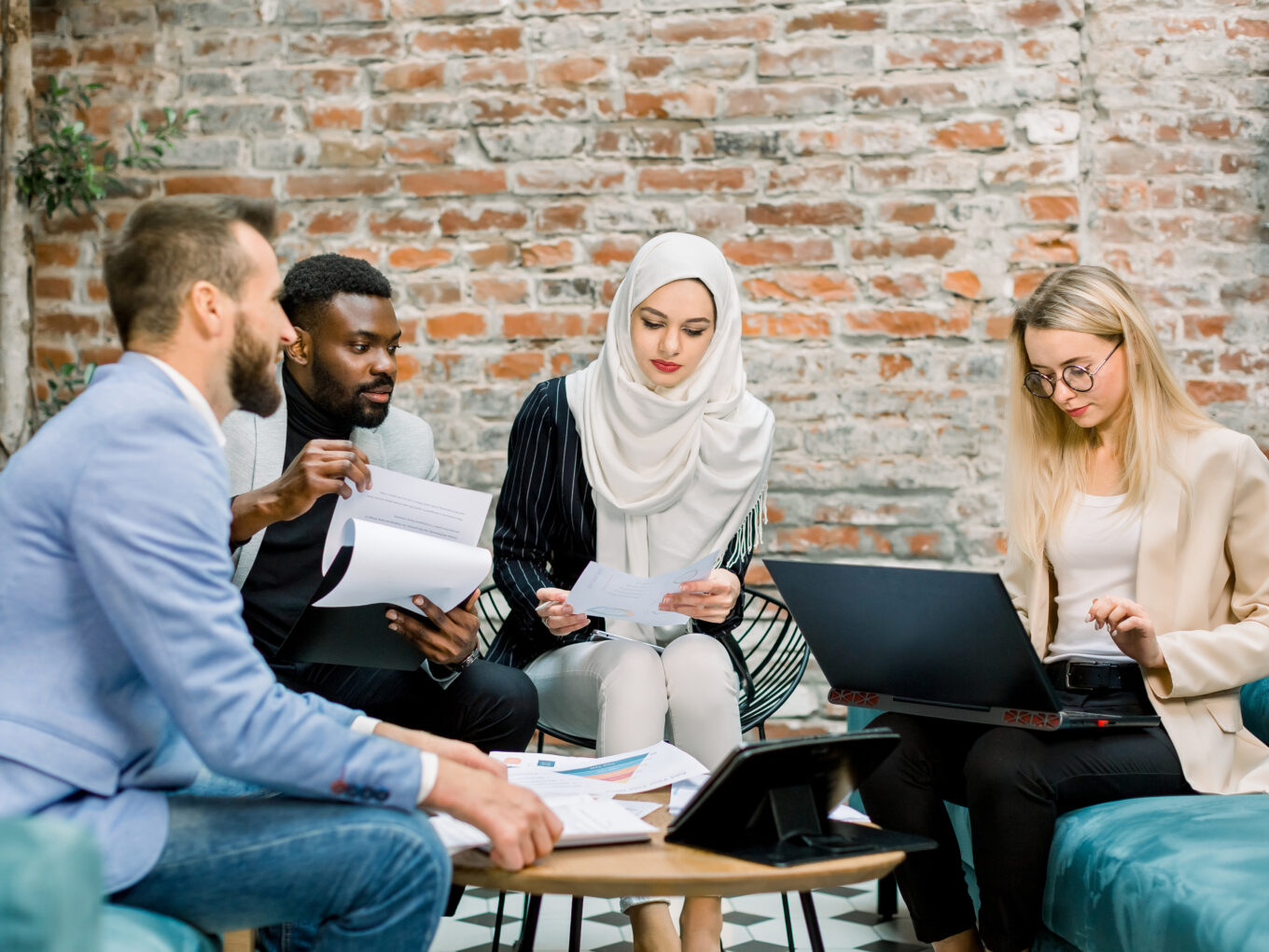 Team meeting with four people reviewing documents and a laptop in a casual setting.