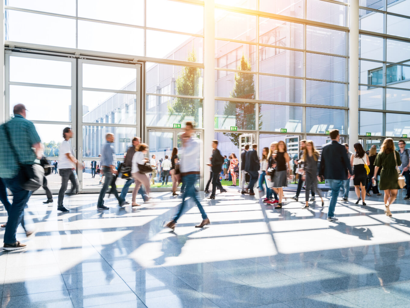Busy lobby with people walking and sunlight streaming through large windows