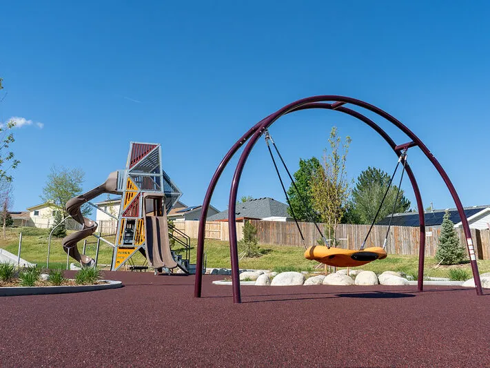 Modern playground with a slide tower, swing, and houses in the background