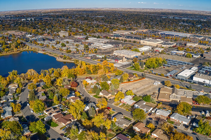 Aerial view of a suburban neighborhood with houses, roads, and a nearby lake surrounded by autumn foliage.