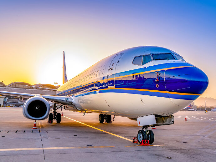 Commercial airplane parked at airport during sunset, with runway lights on