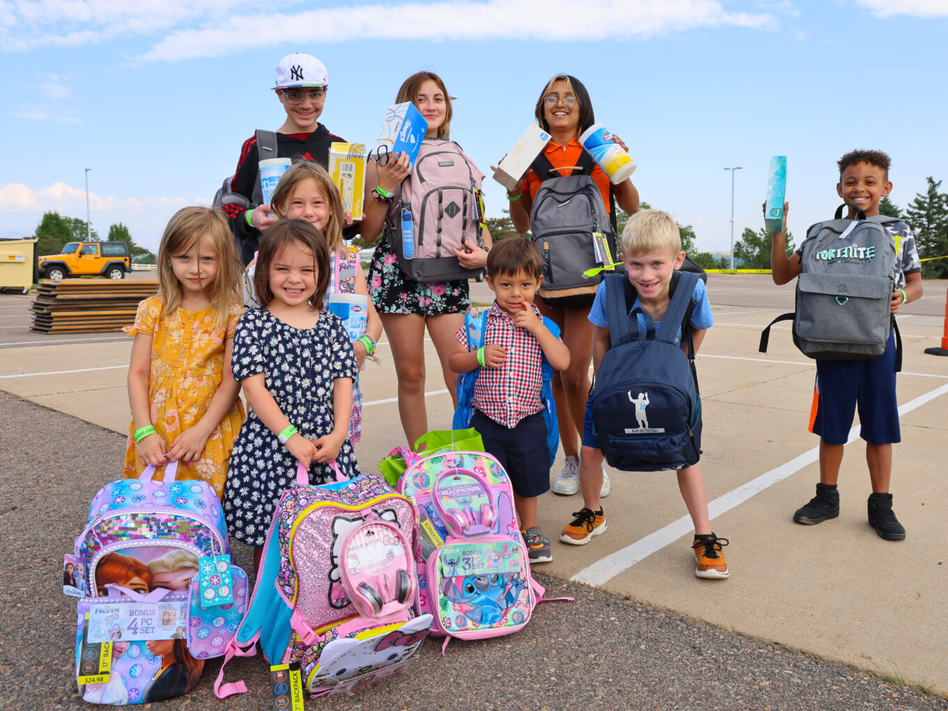 Children holding backpacks and school supplies, smiling at an outdoor event. Fortnite logos visible.