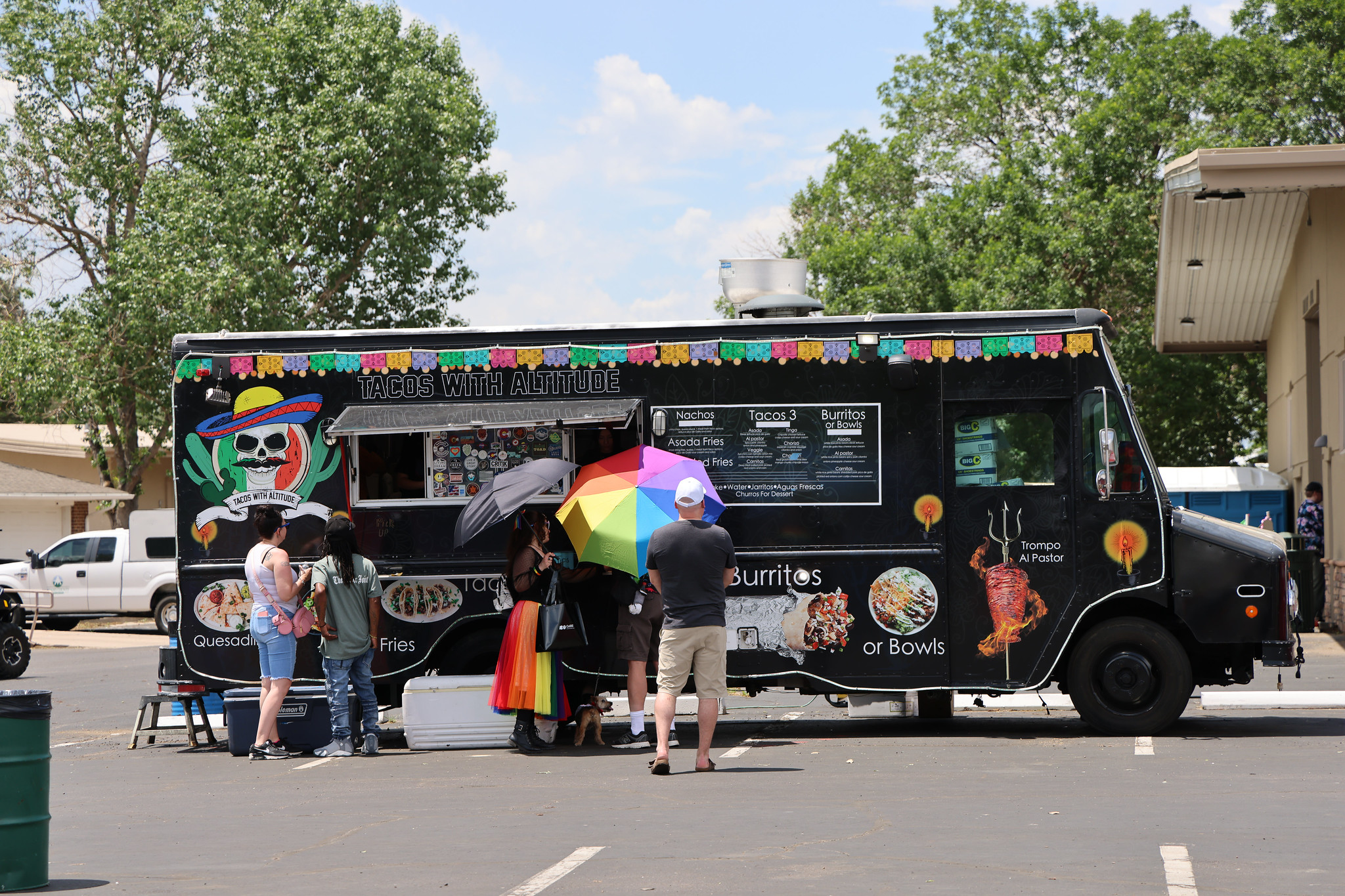 Food truck with "Tacos With Altitude" serving people under colorful umbrellas.