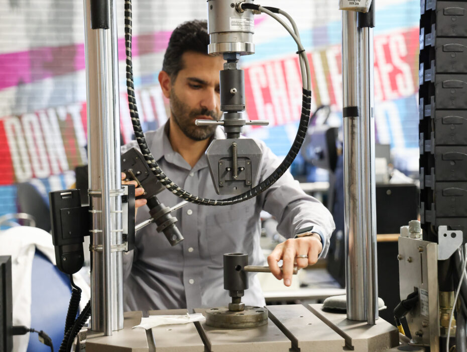 Man operating machinery, adjusting equipment in a workshop, surrounded by colorful wall text.