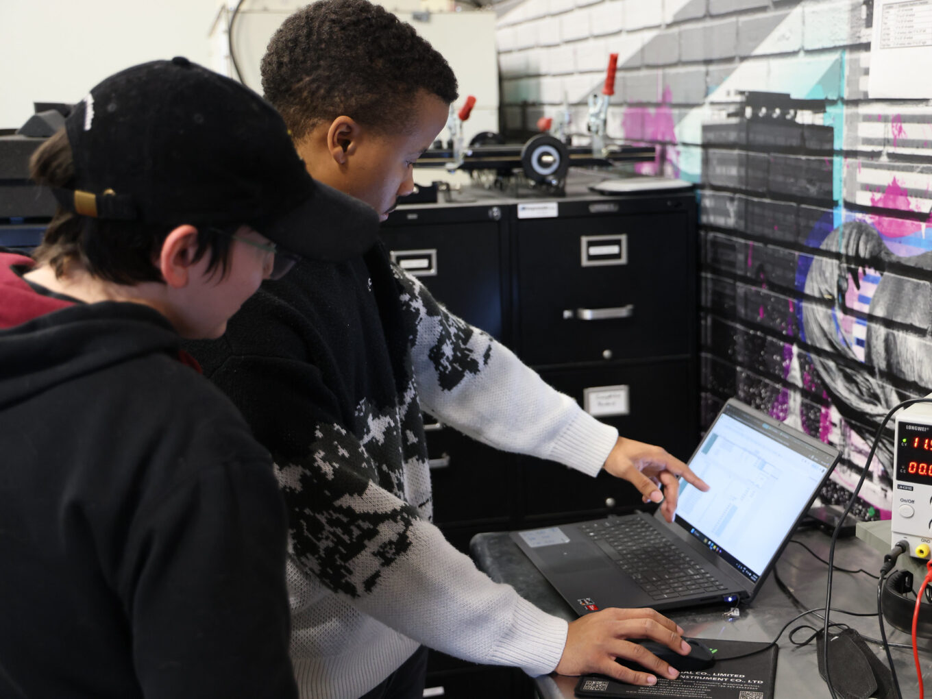 Two people collaborating at a laptop in an industrial workspace.