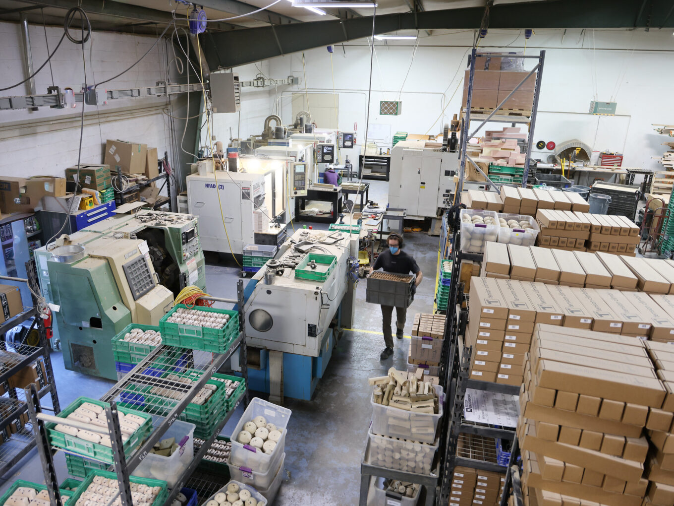 Factory floor with machinery, stacked boxes, and a worker carrying a crate.