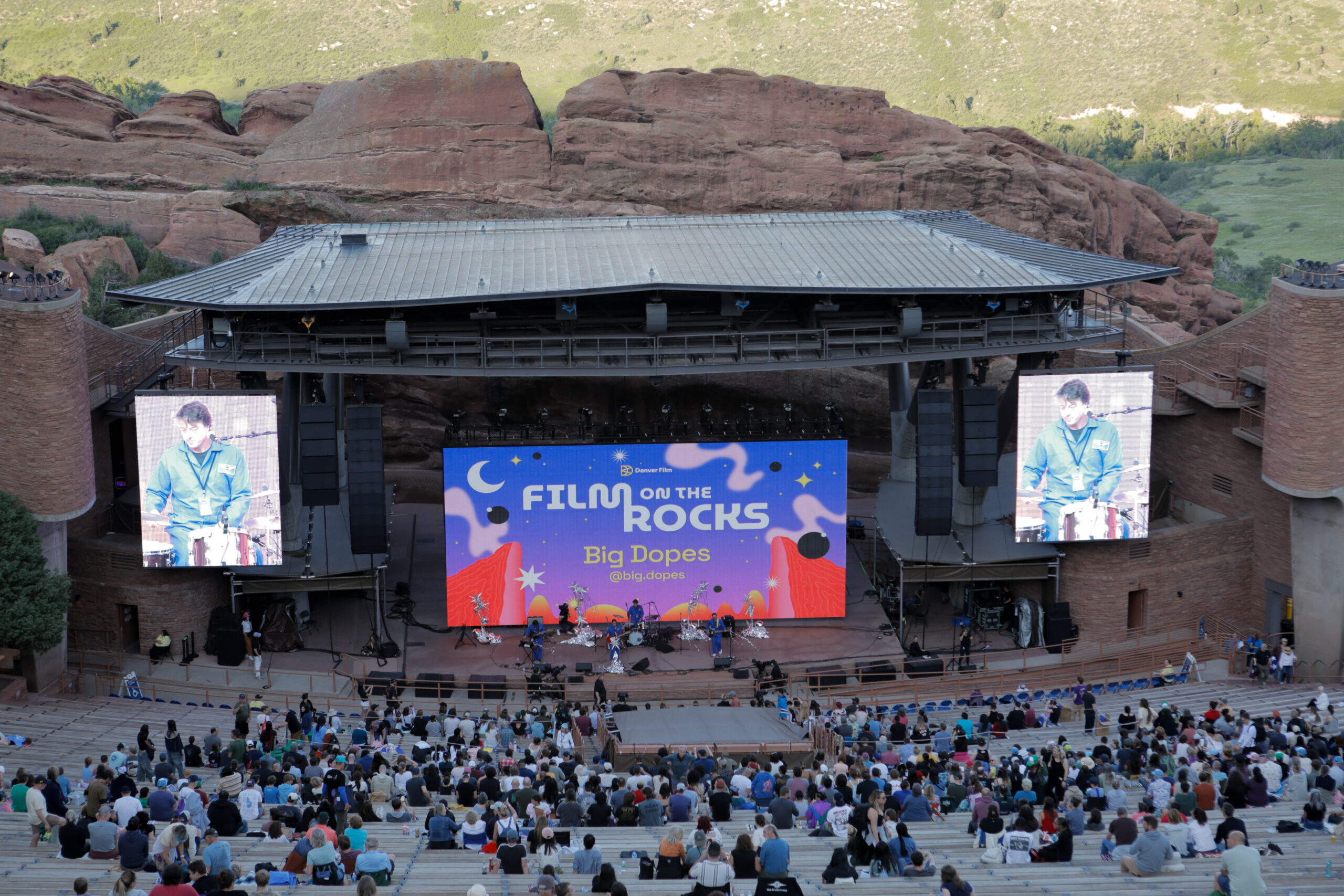 Large outdoor amphitheater featuring "Film on the Rocks" with band Big Dopes performing, surrounded by a scenic rock formation backdrop.