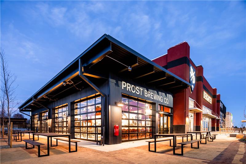 Prost Brewing Co. building at dusk with outdoor seating and modern glass facade