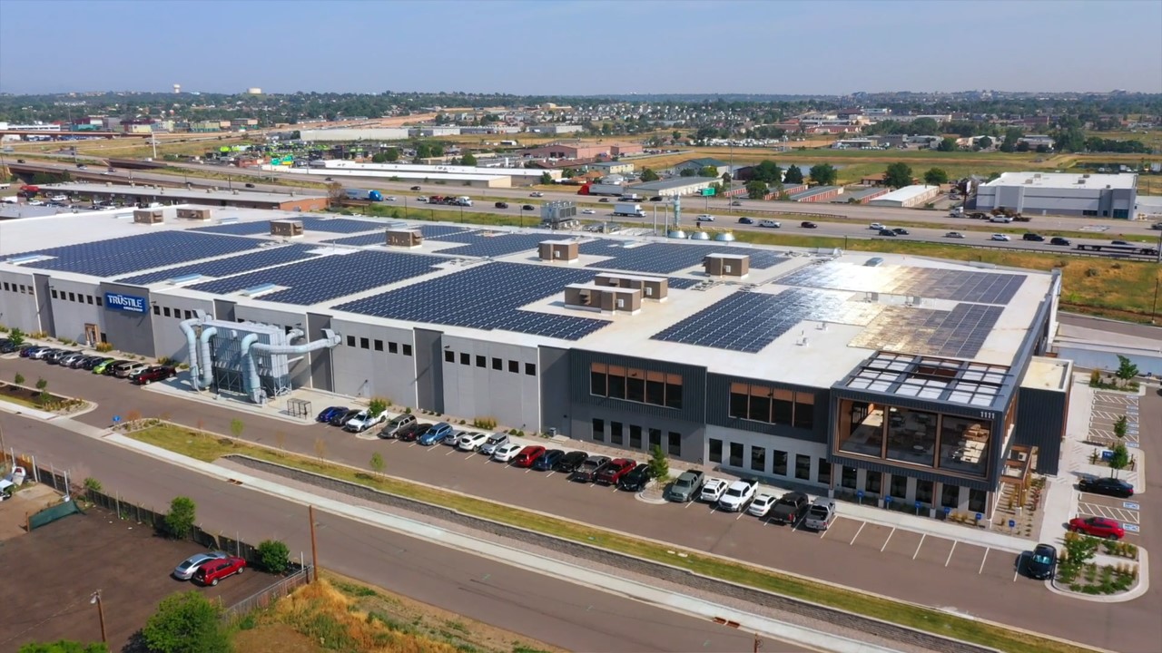 Aerial view of a large building with solar panels, labeled TruStile, surrounded by parking lots and roads.