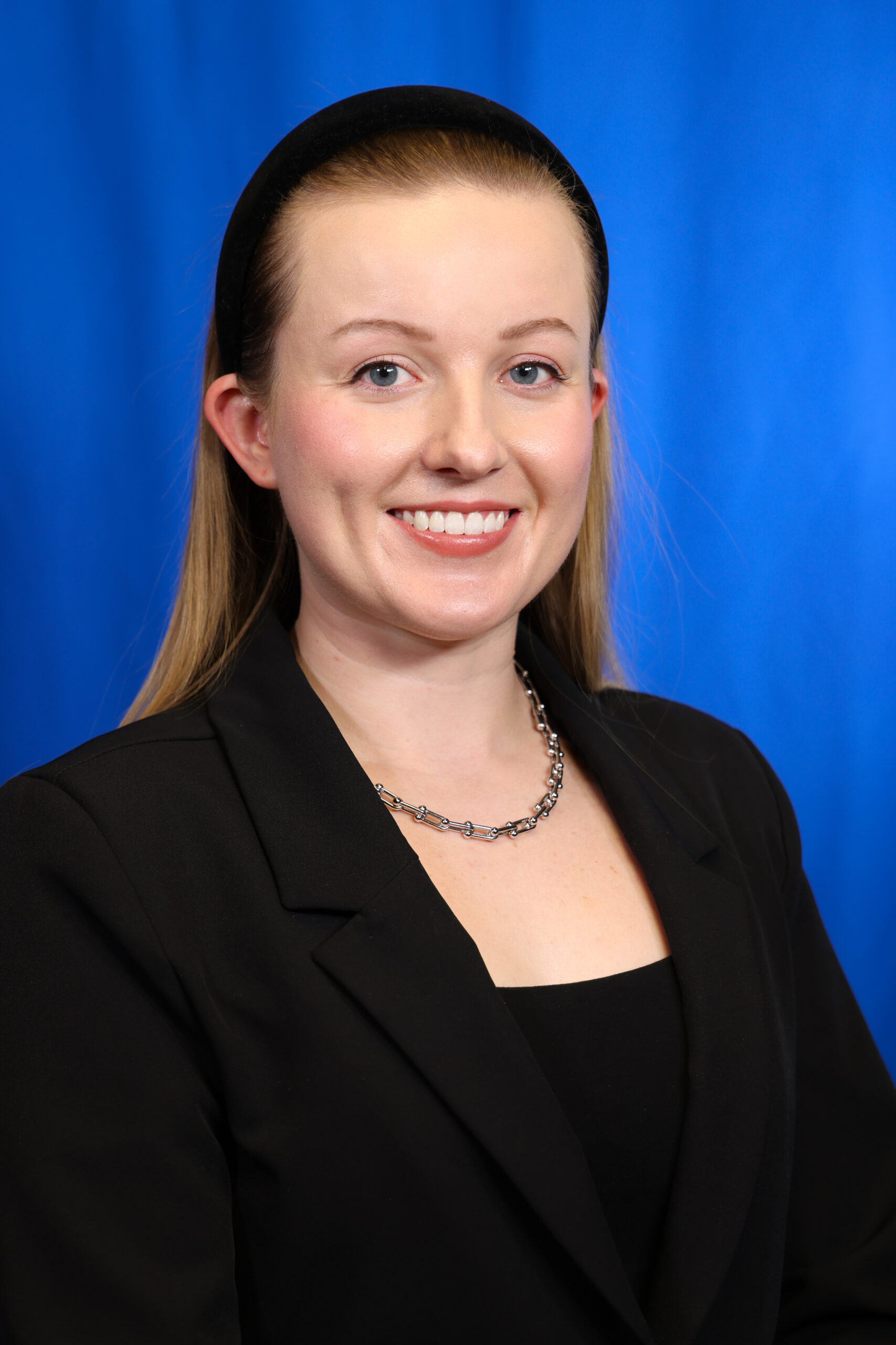 Victoria smiling in a black blazer against a blue background.