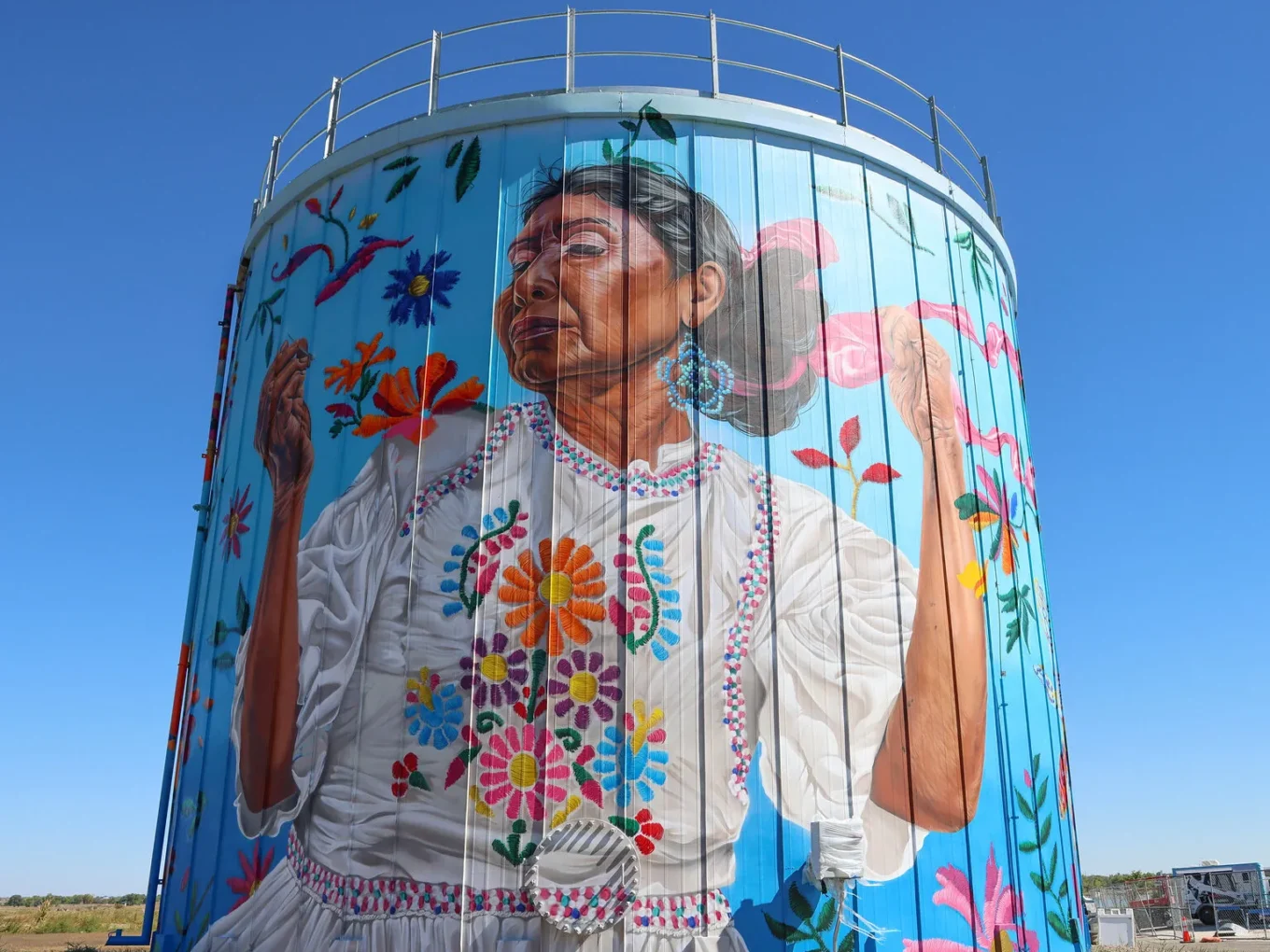 Wall mural of a woman in floral dress celebrating cultural heritage, painted on a cylindrical building.
