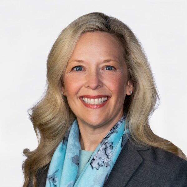 Jenni Hall smiling, wearing a blue floral scarf and gray blazer
