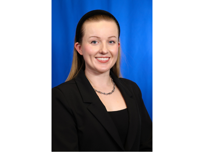 Victoria smiling in a black blazer, blue background.